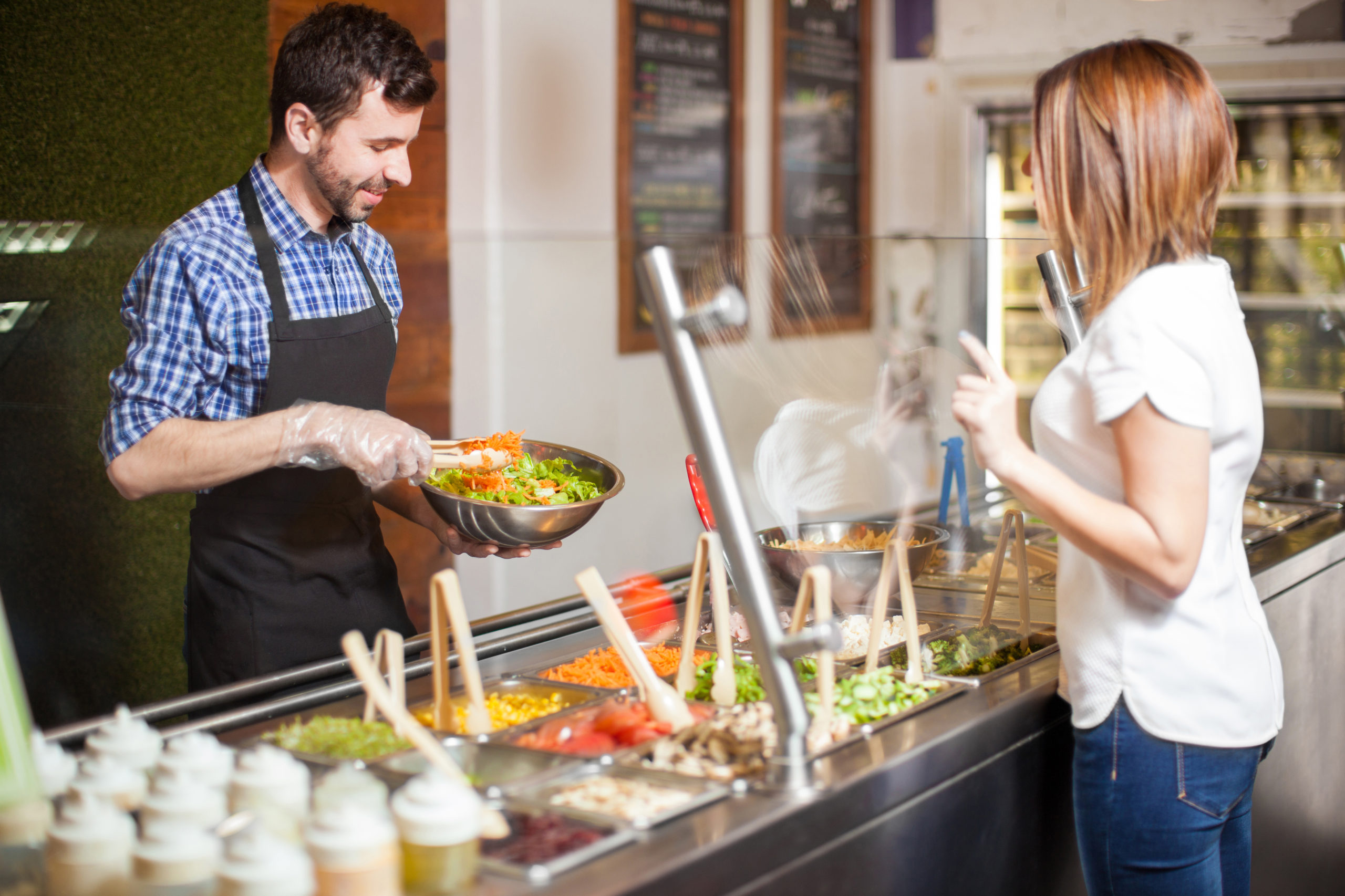 Handsome young man with a beard making a salad for a customer at a restaurant