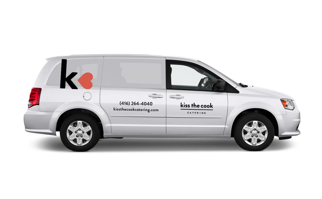 A white van with "kiss the cook CATERING" and contact details on the door. The rear side panel displays a large "k" with a red heart shape as part of the design.